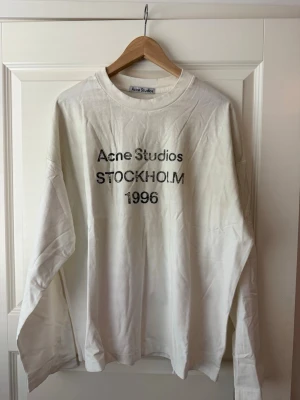 Acne studio sleeve vit M - Vit långärmad t-shirt från Acne Studios med tryck i svart text på bröstet där det står 'Acne Studios STOCKHOLM 1996'. Klassisk rund hals och relaxed fit. Perfekt för dig som gillar minimalistisk och stilren design.