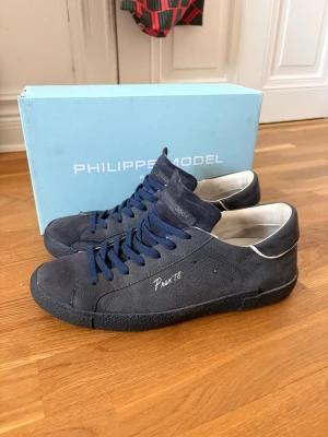 Philippe Model blåa sneakers - Snygga blå sneakers från Philippe Model i mocka med vita detaljer och blå skosnören. Modellen har en låg silhuett och texten 'Prsx 78' på sidan. Insidan är vit. Perfekta för hösten som snart kommer skorna är väldigt sparsamt använda och är i princip i nyskick. 