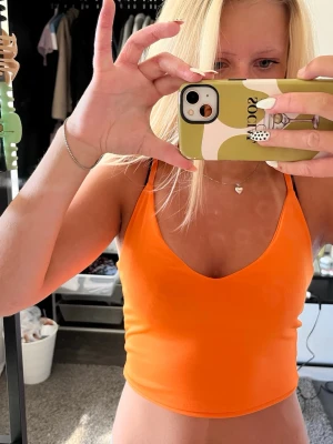 Orange croppad linnetopp - Snygg orange croppad linnetopp med smala axelband och v-ringad hals. Perfekt för varma dagar och enkel att styla med jeans eller kjol. Tunn och mjuk i materialet för en bekväm känsla.