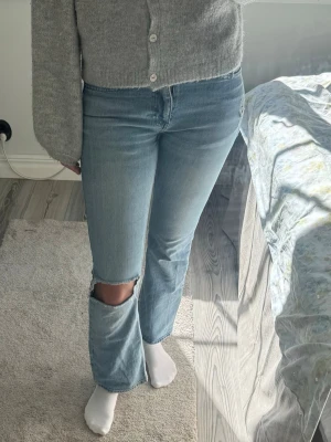 Ljusblå bootcut jeans med hål - Säljer ett par ljusblå bootcut jeans med ett hål vid ena knät och slitningar. Jeansen har klassisk femficksdesign. 