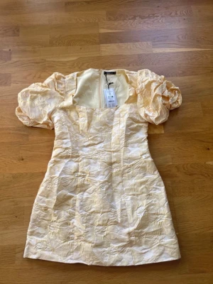 Kort ljusgul klänning Gina Tricot - Supersöt kort klänning från Gina Tricot i ljusgul nyans med puffärmar och strukturmönster. Klänningen har dragkedja bak och är gjord av återvunnen polyester. Perfekt för dig som vill sticka ut med en unik och trendig look.