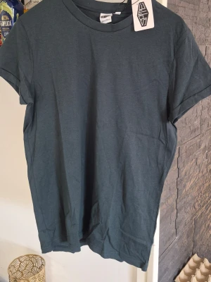 Mörkgrön basic t-shirt - En enkel och stilren mörkgrön t-shirt i mjuk bomull. T-shirten har rund halsringning och korta ärmar, perfekt för en avslappnad look. Passformen är normal och tyget känns skönt mot huden.