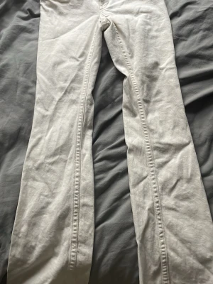 Vita utsvängda jeans med fickdetaljer - Säljer ett par vita jeans med utsvängda ben och snygga fickdetaljer bak med silverfärgade knappar. Jeansen har medel midja och är gjorda i ett klassiskt denimtyg. Perfekta för dig som vill ha en clean och trendig look.