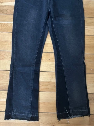 Svarta utsvängda jeans från gallery dept - Säljer ett par svarta jeans med utsvängda ben och råa, avklippta benslut. Jeansen har en mörk tvätt och klassisk femficksmodell. Perfekta för dig som gillar en trendig och avslappnad stil.