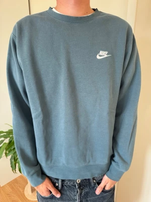 Blå crewneck sweatshirt från Nike - Snygg blå crewneck sweatshirt från Nike med klassisk vit logga på bröstet. Tröjan har rund halsringning, långa ärmar och ribbade muddar vid ärmslut och nederkant. Perfekt för en avslappnad och sportig stil.