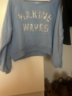 Ljusblå sweatshirt från Hollister - Ljusblå sweatshirt från Hollister med texten 'MAKING WAVES' i vitt och mönstrade bokstäver. Tröjan har rund halsringning och långa ärmar. 