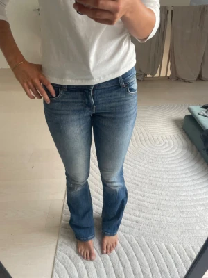 Bershka jeans - Säljer ett par klassiska blå bootcut jeans med mellanblå tvätt och lätt slitning på låren. Jeansen har normal midja, fem fickor och dragkedja med knapp. Perfekta för en avslappnad och trendig look.