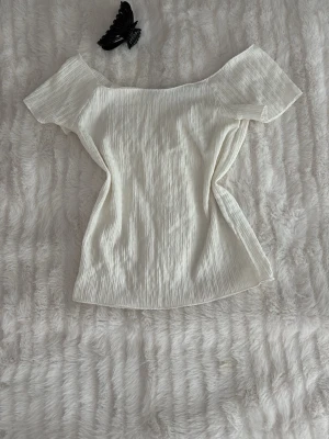 Vit offshoulder topp från 157 - Säljer en vit offshoulder topp från 157 i storlek XS. Toppen har en ribbad struktur och är tillverkad i ett lätt material som ger en snygg passform. Perfekt till jeans eller kjol för en fräsch look.
