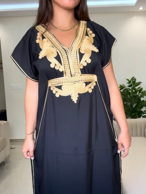 Gandoora🖤 - Elegant svart kaftanklänning med detaljerade broderier i guld längs v-ringningen och midjan. Klänningen har korta ärmar och en loose passform som ger en avslappnad men stilren look. Perfekt för dig som vill sticka ut med snygga detaljer.
