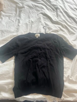 Svart kortärmad topp från H&M - En enkel och stilren svart topp från H&M med korta ärmar och rund halsringning. Materialet känns mjukt och bekvämt, perfekt för att matcha med jeans eller kjol. Passformen är normal och toppen har en klassisk look.