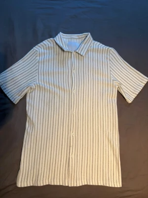 Beige kortärmad skjorta - Beige randig kortärmad skjorta med mjukt material perfekt för sommaren, knappt använd och i väldigt bra skick. Från Lager 157 i storlek S