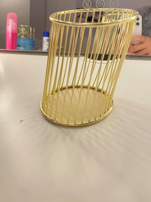 Guldfärgad pennhållare i metall - Säljer en stilren pennhållare i guldfärgad metall med rund botten och öppet gallerdesign. Perfekt för skrivbordet för att organisera pennor, borstar eller andra småprylar. Modern och enkel look som passar in i de flesta rum.
