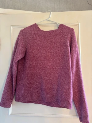 Lila stickad tröja med rund hals - Mysig lila/rosa stickad tröja med rund halsringning och långa ärmar. Tröjan har en rak passform och ribbstickade muddar vid ärmslut och nederkant. Perfekt för kalla dagar nu i höst.