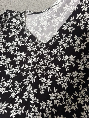 Svart blommig topp med v-ringning - Söt svart topp med vitt blommönster och v-ringning. Toppen har rynkade detaljer framtill och halvlånga ärmar. Aldrig använd så den är i nyskick💕