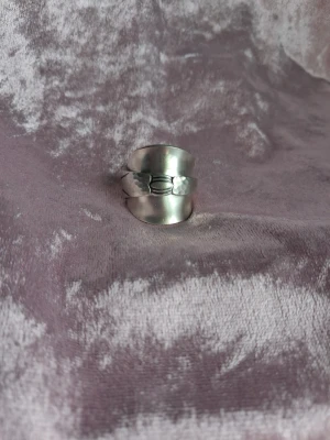Skedring nysilver 19/59 - Unik silvrig ring i form av en böjd sked, med detaljerad dekor framtill. Ringen har en bred, justerbar design och en blank finish som ger en cool retrovibe. Perfekt för dig som gillar statement-smycken och vill sticka ut. Storlek 19/59 