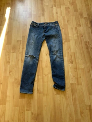 Blå replay jeans - Säljer ett par blå jeans med raka ben och slitningar på båda knäna. Klassisk femficksmodell och detaljerade sömmar på bakfickorna.