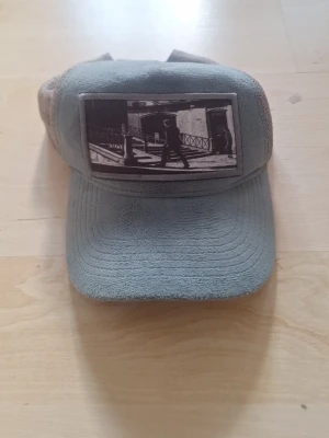 Grön meshkeps med fototryck - Säljer en grön keps med mesh på sidorna och ett svartvitt fototryck framtill. Kepsen har böjd skärm och justerbar rem bak. Perfekt för dig som vill ha en unik och stilren accessoar till vardagslooken.