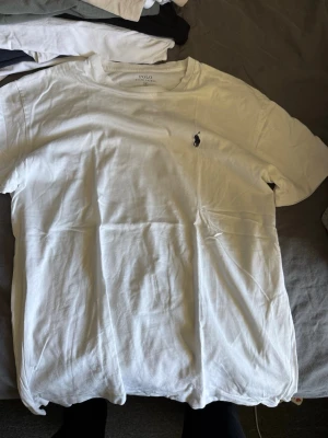 Vit t-shirt från Polo Ralph Lauren - Klassisk vit t-shirt från Polo Ralph Lauren med rund halsringning och den ikoniska broderade loggan på bröstet. Tillverkad i mjuk bomull för en skön och avslappnad känsla. Perfekt basplagg för alla tillfällen.