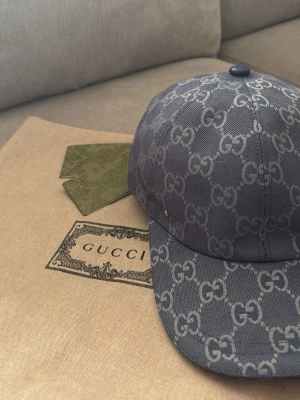 Mörkblå Gucci keps med GG-mönster - Snygg mörkgrå keps från Gucci med det klassiska GG-monogrammet över hela kepsen. Tillverkad i ett slitstarkt tygmaterial och har en böjd skärm. Perfekt accessoar för dig som vill ha en exklusiv och trendig look.