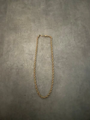 Guldtonat kedjehalsband - Snyggt halsband i guldtonad metall med tvinnad kedja som ger en cool och trendig look. Perfekt att bära som statement-piece till olika outfits. Låset är diskret och smidigt. Passar dig som gillar stilrena accessoarer.