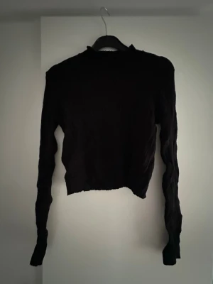 Svart ribbad tröja  - En svart ribbad tröja från BikBok med lång ärm och hög hals. Tröjan har en croppad passform och är tillverkad i ett stretchigt material. Säljer då den inte kommer till användning.
