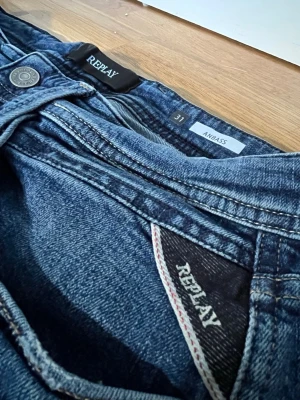 Blå Replay Anbass Jeans - Säljer ett par klassiska blå Replay jeans med raka ben och snygga kontrastsömmar. Jeansen har fem fickor och detaljerade bakfickor. Perfekta till en avslappnad stil och passar till det mesta i garderoben.