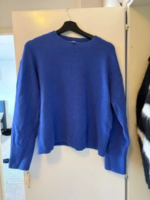 Kornblå stickad tröja - En kornblå stickad tröja med rund halsringning och breda ribbade muddar vid ärmslut och nederkant. Tröjan har en avslappnad passform och är perfekt för lager på lager. Materialet ser mjukt och bekvämt ut.