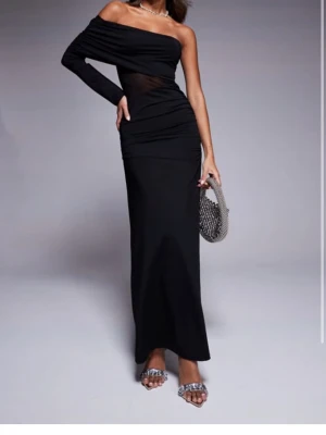 Svart oneshoulder långklänning - Snygg svart långklänning med oneshoulder-design och en lång ärm. Klänningen har en transparent meshdetalj i midjan som ger en extra edge. Perfekt för dig som vill sticka ut med en elegant och modern look. Helt ny och aldrig använd från ASOS, prislappen är borta men orginalförpackningen finns kvar! Nypris 459 kr