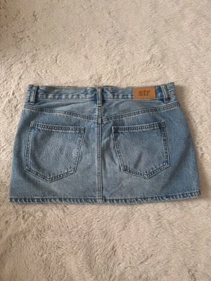 Blå jeanskjol  - Säljer en klassisk blå jeanskjol i kort modell med två bakfickor och bälteshällor. Kjolen har en enkel design och är gjord i ett slitstarkt denimtyg. Aldrig använd💕 Skriv för mer info