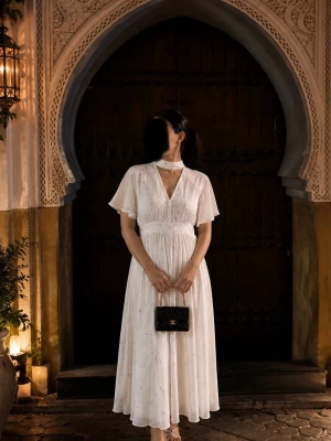 Vit långklänning med blommigt mönster - Romantisk vit långklänning med små blommor i lila och blått. Klänningen har v-ringning, korta vida ärmar och markerad midja. Tillverkad i ett mjukt, lätt material som faller snyggt. Perfekt för sommarens alla tillfällen.