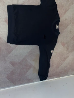 Svart sweatshirt med rund hals - En enkel svart sweatshirt med rund hals och långa ärmar. Tröjan har en liten patch på ena ärmen och ribbade muddar vid ärmslut och nederkant. Perfekt till ett avslappnat streetwear-look. Det går ej skanna den men den är äkta