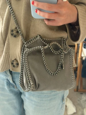  Stella McCartney  väska - Säljer en grå Stella McCartney Falabella handväska  mockamaterial. Perfekt storlek för det viktigaste och kan bäras både crossbody och i handen. Den har använts cirka 3 gånger och har inga defekter och är i princip ny skick🥰 vid fler frågor är det bara att ställa.