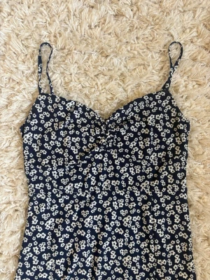 Gina tricot Blommig långklänning med slits - Mörkblå långklänning med vita blommor och smala axelband. Klänningen har en snygg slits framtill och figurnära passform. Perfekt för sommarens alla tillfällen och har ett lätt, luftigt tyg. Väldigt skönt material, storlek S. Använd bara 1 gång. 