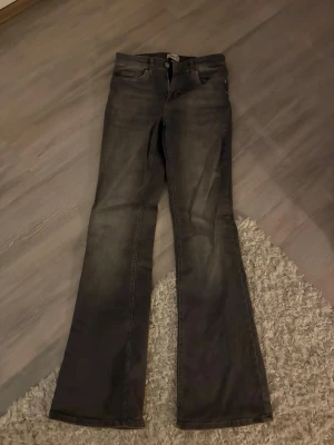 Grå bootcut jeans med hög midja - Säljer ett par gråa bootcut jeans med hög midja och klassisk femficksdesign. Jeansen har utsvängda ben och är tillverkade i ett stretchigt denimtyg som ger en snygg passform. Perfekta för dig som gillar en retroinspirerad look.