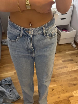 Ljusblå raka jeans - Säljer ett par ljusblå mom jeans med hög midja och raka ben. Klassisk femficksmodell med bälteshällor och knappgylf. Jeansen är i ett mjukt denimtyg som ger en avslappnad och trendig look.