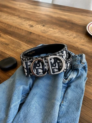 Svartvitt bälte  - Snyggt svartvitt bälte med tydligt spänne i silver. Bältet har ett grafiskt mönster och bred design som gör det till en statement-accessoar. Perfekt för att lyfta vilken outfit som helst.