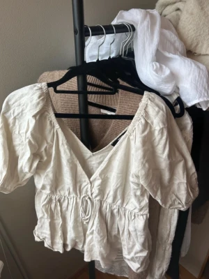 Beige omlottopp från BikBok - Söt beige omlottopp från BikBok i storlek XS. Toppen har korta puffärmar, v-ringning och en knytning framtill. Tillverkad i ett lätt och luftigt material, perfekt för varmare dagar.