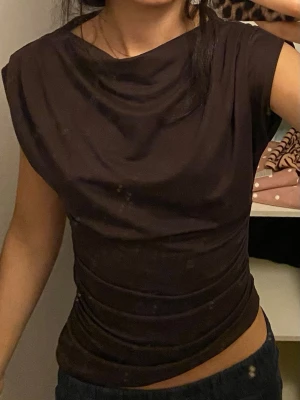 Brun draperad topp med kort ärm från HM - Snygg brun topp med draperad halsringning och tight passform. Toppen har korta ärmar och är tillverkad i ett mjukt, stretchigt material som formar sig efter kroppen passar storlek xs/s💕