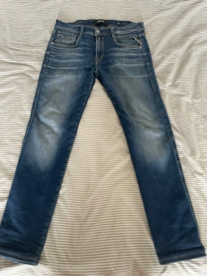 Blå Replay jeans - Säljer ett par blå jeans från Replay. Klassisk femficksmodell med raka ben och normal midja. Jeansen har en cool, avslappnad look och är tillverkade i denim. Jensen är köpta på jeans bolaget och är uppsydda så benen är 90 cm från midjan och ner! Storlek 28 i midjan.