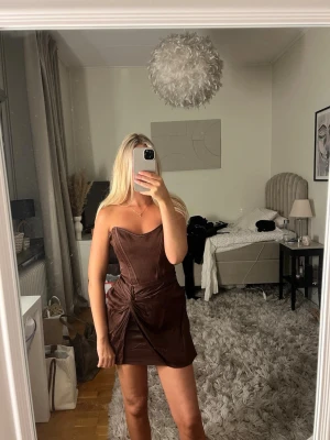 Brun axelbandslös kort klänning - Säljer en brun axelbandslös kort klänning med omlottdetalj och drapering i midjan. Från Zara storlek S