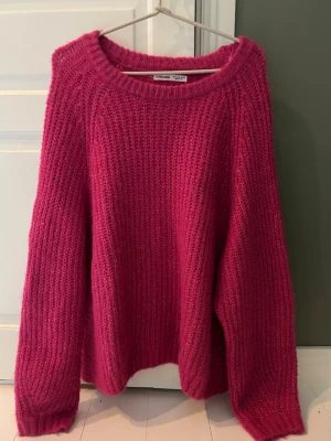 Rosa stickad oversized tröja - Mysig stickad tröja i en stark rosa färg med grovstickad struktur och avslappnad, oversized passform. Tröjan har rund halsringning och långa ärmar. Perfekt för att hålla värmen under kyliga dagar. Eftersom att den är overzised så passar den även M och L