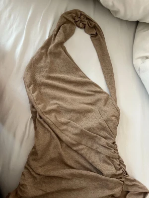 Beige oneshoulder klänning ASOS - Trendig beige oneshoulder klänning från ASOS DESIGN. Klänningen har en snygg drapering och knutdetalj vid axeln som ger en unik look. Tillverkad i mjukt material som sitter skönt mot kroppen. Perfekt för dig som vill sticka ut med en stilren och modern outfit.