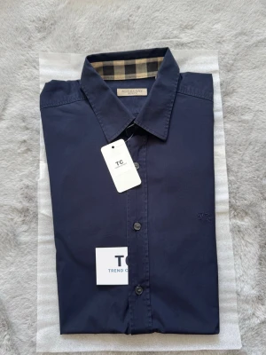 Burberry skjorta  - Super fin marinblå burberry skjorta i storlek XL, skjortan är i mycket fint skick utan några defekter. Burberry mönstret finns på båda ärmsluten och även runt om kargens indsida.. Nypris 5000kr mitt pris endast 1200kr. Hör av er vid frågor. Mvh Trend closet🙌