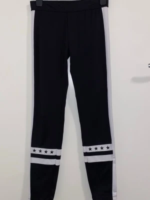 Svarta leggings med vita ränder och stjärnor - Snygga svarta leggings med vita sidopaneler och dubbla vita ränder längst ner på benen. Dekorerade med svarta stjärnor på de vita ränderna vid bensluten. Stretchigt material och hög midja för skön passform. Perfekta till en sportig eller avslappnad look.