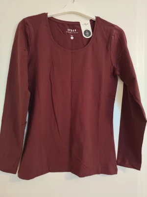 Mörkröd långärmad topp - En enkel och stilren mörkröd långärmad topp med rund halsringning. Tillverkad i mjuk bomull som känns skön mot huden. Perfekt att matcha med jeans eller kjol för en clean look.