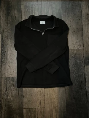 Svart halvzip tröja med krage - Stilren svart långärmad tröja med halv dragkedja och klassisk krage. Tröjan har en bröstficka på vänster sida och är tillverkad i ett mjukt material som passar perfekt till en avslappnad look. Använd 2-3 gånger bara så den är nyskick.