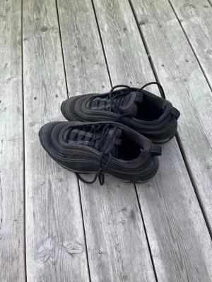 Svarta sneakers med vågig design - Säljer ett par helsvarta sneakers med vågiga detaljer och synlig luftbubbla i sulan. Skorna har snörning och en sportig look, perfekta för dig som gillar streetwear och bekväma skor till vardags. Materialet är en mix av textil och syntet.