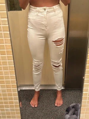 Vita ripped jeans Pull&Bear - Säljer ett par vita high waist jeans från Pull&Bear i storlek 36. Jeansen har skinny fit och flera stora slitningar på båda benen för en trendig, avslappnad look. Tillverkade i stretchigt denim-material som sitter snyggt och bekvämt.