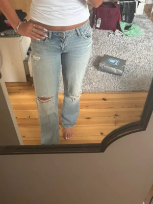 Ljusblå lågmidjade jeans från Zara - Säljer ett par ljusblå raka jeans med låg midja och slitningar på knäna. Jeansen är nya med prislapp och storlek 36!