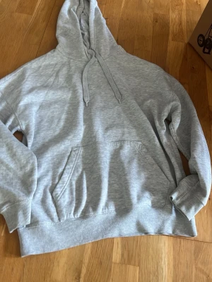 Ljusgrå hoodie från FB Sister - Ljusgrå hoodie från FB Sister i storlek XS. Klassisk modell med huva och dragsnören, stor magficka framtill och ribbade muddar vid ärmar och nederkant. Tillverkad i mjukt och bekvämt material, perfekt för en avslappnad stil.